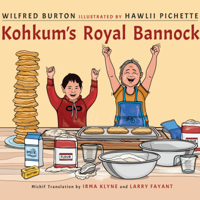 This image is the cover of the book "Kohkum's Royal Bannock" by Wilfred Burton, illustrated by Hawlii Pichette; translated into Michif by Irma Klyne and Larry Fayant. The image has a drawing of a boy and his kohkum, with their arms raised in triumph, standing behind a table filled with ingredients for making bannock. Beside them is a stack of all the bannock they made for the royal visit!